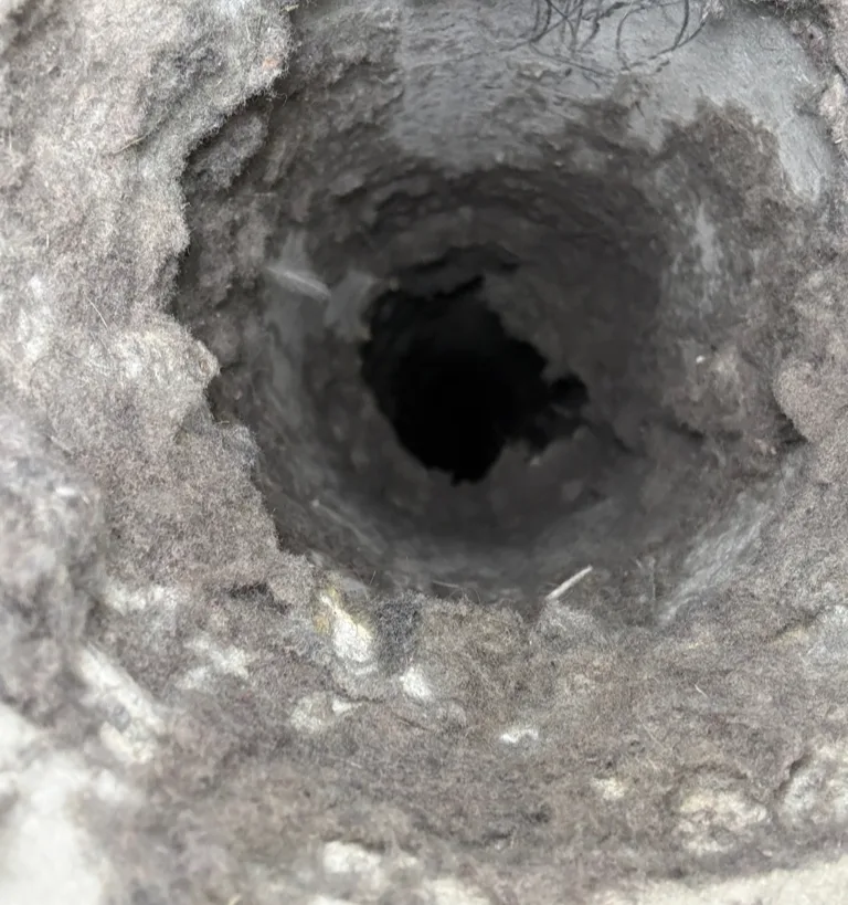 Dryer vent opening clogged with lint behind a Maytag dryer