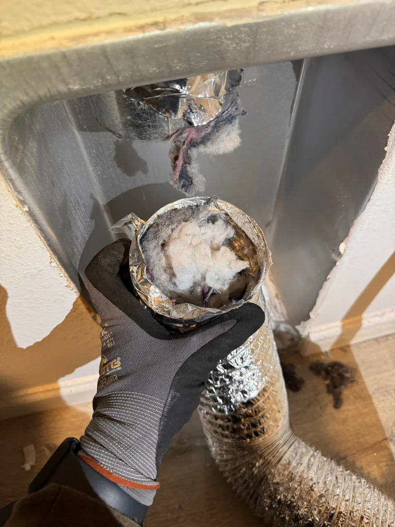 Lint-clogged foil dryer vent duct pulled from behind a Whirlpool dryer