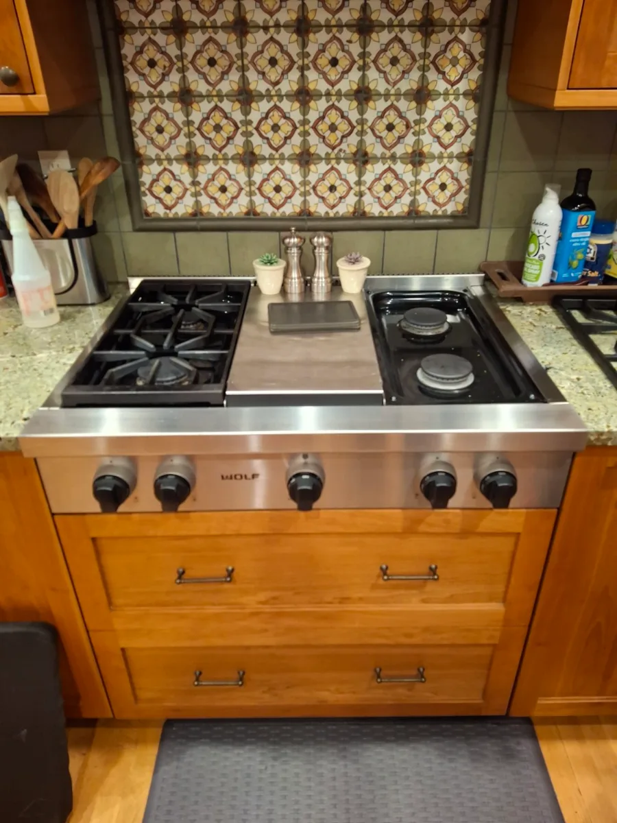 Wolf gas rangetop with a griddle set in tile and wood cabinets